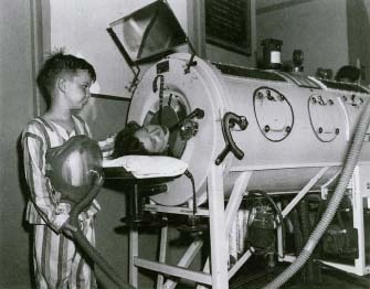 This photograph, taken in 1949, shows an 8-year-old boy with polio wearing the newly introduced one-pound portable "Monaghan" iron lung around his chest. He is standing next to an adult woman lying confined in an old-style iron lung. Dennis Burke, Daily Mirror/Corbis-Bettman